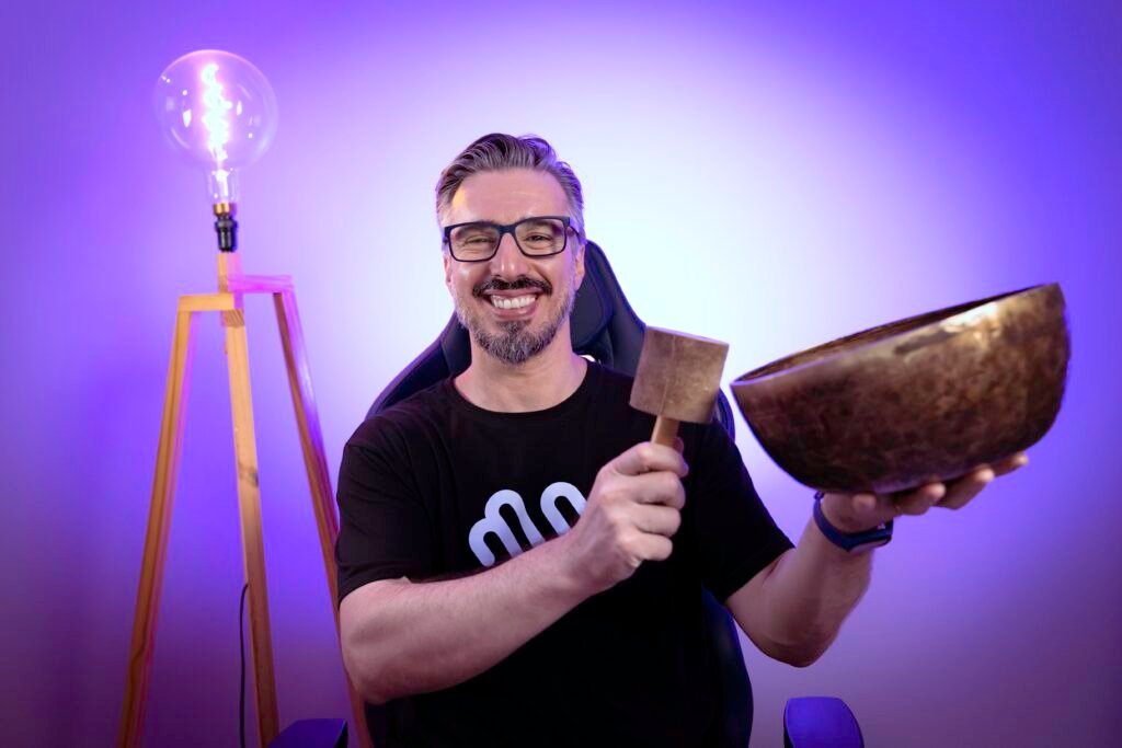 Charles Betito sorrindo, segurando um mallet de madeira e uma tigela tibetana.